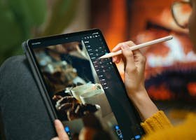 A person editing photos on a tablet with a stylus by a cozy fireplace setting.